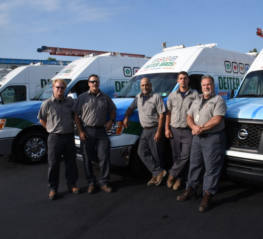 Group of HVAC technicians standing in front of branded service vans in a parking lot on a sunny day.
